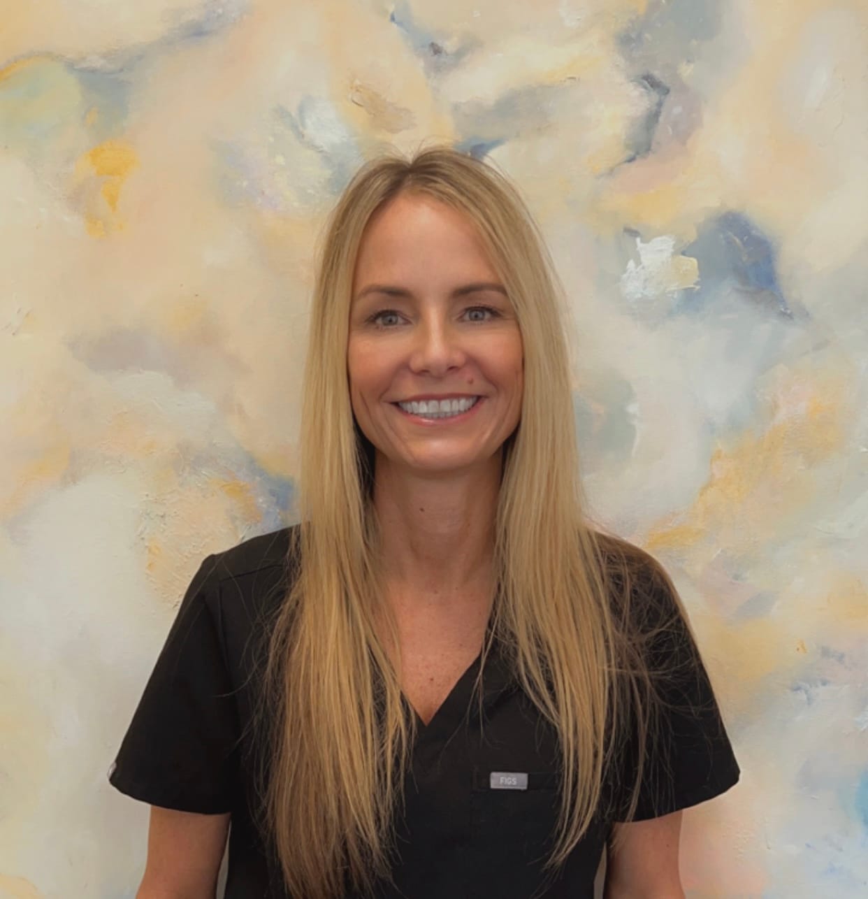 About - Edward Love MD Karrie Hogan, RN BSN, smiling in black scrubs against a soft, abstract background, representing the welcoming face of Dr. Edward J. Love's plastic surgery practice.